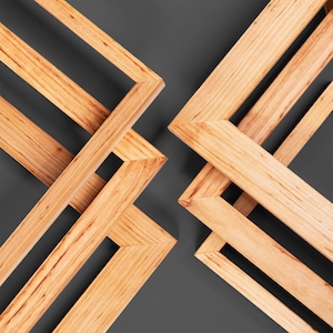May include: Geometric wooden frames arranged in a symmetrical pattern against a dark gray background. The frames are made of light-colored wood, with visible grain and angled corners. The design creates a modern, abstract aesthetic.