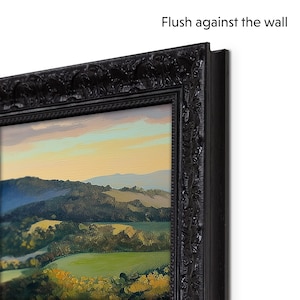 May include: A black framed landscape painting of a green valley with hills in the distance. The painting is framed with a decorative black frame with a raised edge. The text "Flush against the wall" is visible in the upper right corner of the image.
