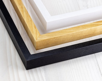 Puede incluir: Tres marcos de fotos, uno negro, uno de madera natural y uno blanco, están apilados uno encima del otro. Los marcos son todos rectangulares y tienen un diseño sencillo.