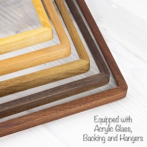 Könnte beinhalten: Vier Holzbilderrahmen in verschiedenen Brauntönen, übereinander gestapelt. Die Rahmen sind aus massivem Holz gefertigt und haben eine glatte Oberfläche. Ausgestattet mit Acrylglas, Rückwand und Aufhängern.