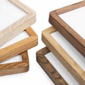 Puede incluir: Primer plano de cuatro marcos de fotos de madera en varios tonos de marrón y beige. Los marcos tienen un diseño simple y moderno con líneas limpias y un acabado de veta de madera natural. Los marcos están vacíos, con espacio blanco visible.