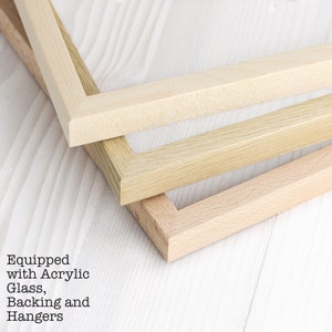 May include: Three wooden picture frames in different shades of wood. The frames are stacked on top of each other, with the lightest wood frame on top. The frames are all made of solid wood and have a smooth finish.