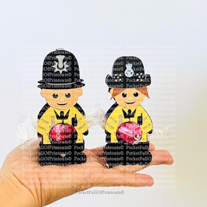 May include: Two small, cartoon-style figurines of police officers, one male and one female, holding red candy eggs. The figurines are wearing black and yellow uniforms with white accents. The background is white.