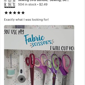以下が含まれることがあります： 白い木製の看板に「You Use My Fabric Scissors I Will Cut You」という文字が青と黒で書かれています。看板は白と黒の星柄の壁に掛けられています。看板には5組のハサミがフックに掛けられています。
