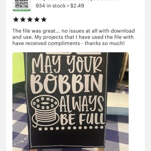 以下が含まれることがあります： 「May Your Bobbin Always Be Full」と白文字で書かれた黒い看板。看板には糸巻きが白くシルエットで描かれている。看板は木製のスタンドに置かれ、青と白の市松模様の表面の上に置かれている。