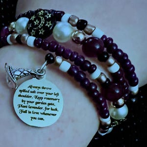 Può includere: Bracciale a più fili con perline viola, bianche, dorate e nere. Un ciondolo d'argento con la scritta: "Always throw spilled salt over your left shoulder..." Un gioiello.