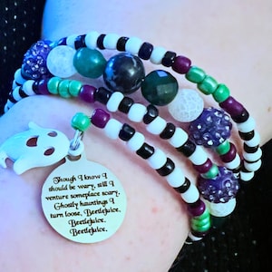 May include: Multi-strand bracelet with white and black beads, purple and green beads, and a charm with the text "Though I know I should be wary, still I venture someplace scary. Ghostly hauntings I turn loose, Beetlejuice. Beetlejuice. Beetlejuice."
