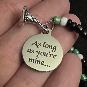May include: A silver charm bracelet featuring a silver charm inscribed with the words "As long as you're mine..." and a silver snake charm. The bracelet is crafted with black, white and green beads.