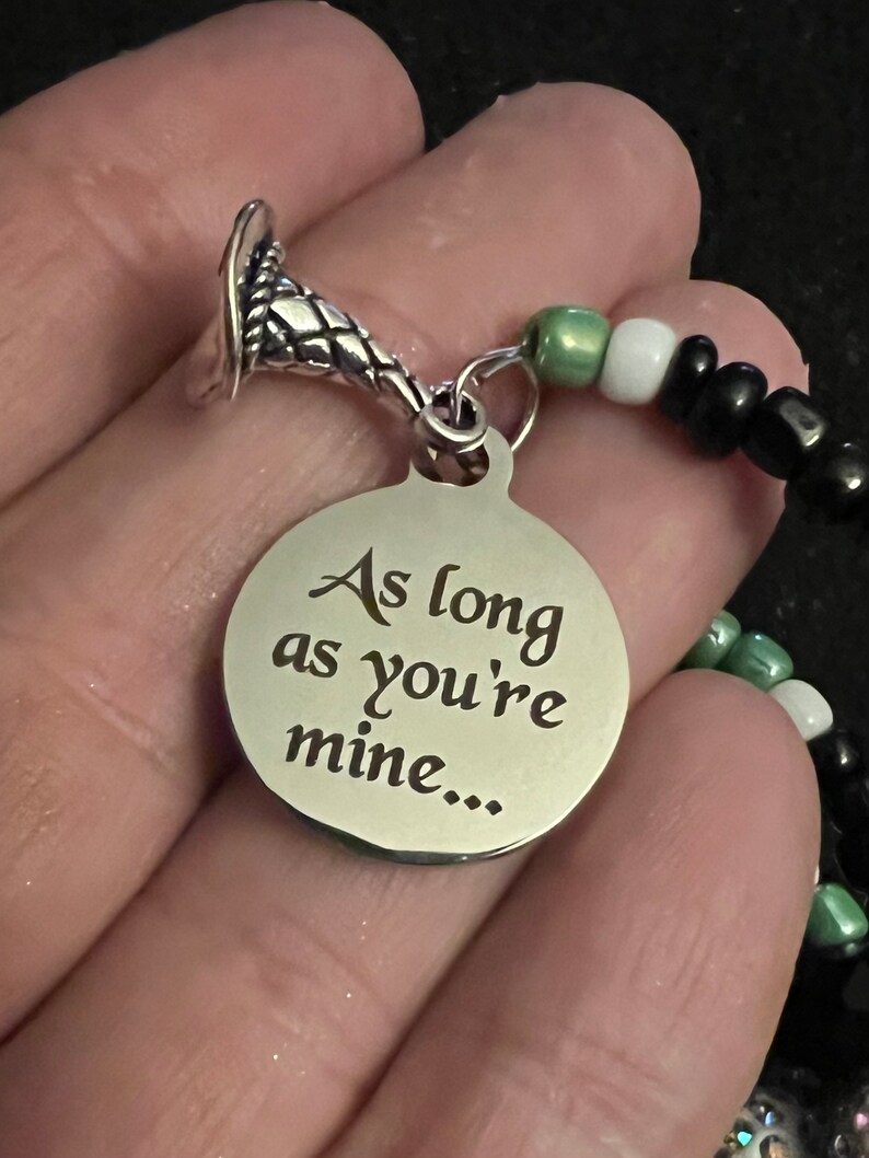 May include: A silver charm bracelet featuring a silver charm inscribed with the words "As long as you're mine..." and a silver snake charm. The bracelet is crafted with black, white and green beads.