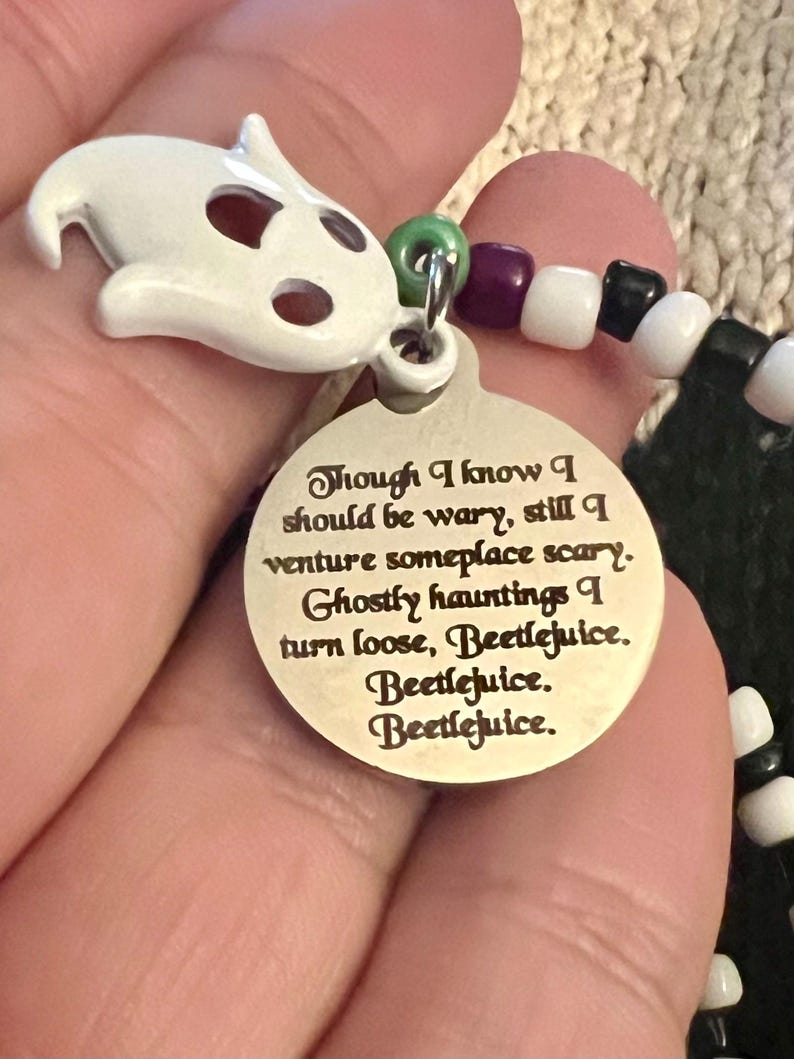 May include: A silver charm with a white ghost charm attached to a beaded bracelet. The charm has an inscription that reads "Though I know I should be wary, still I venture someplace scary. Ghostly hauntings I turn loose, Beetlejuice. Beetlejuice. Beetlejuice."