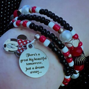 May include: A multi-strand beaded bracelet featuring black, white, and red beads, a Minnie Mouse charm, and a round silver-toned metal pendant engraved with the text: There's a great big beautiful tomorrow, just a dream away...
