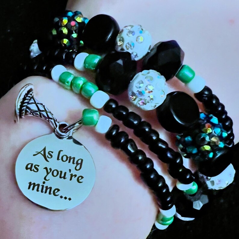 May include: A multi-strand bracelet featuring black and green beads, a silver charm inscribed with the words "As long as you're mine..." and a silver charm shaped like a horn.