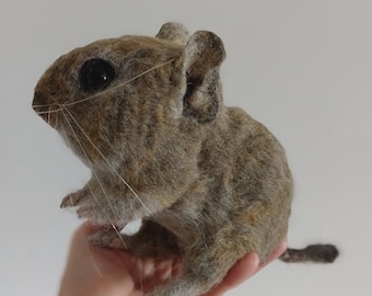 May include: A brown and gray needle felted rodent with a long tail. The rodent is sitting on a person's hand.