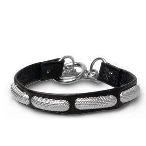 May include: A black leather bracelet with silver accents. The bracelet has three silver oval-shaped embellishments and a silver clasp.