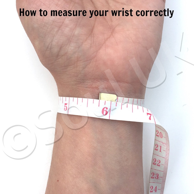 May include: A white measuring tape wrapped around a wrist to show how to measure wrist size correctly. The tape reads 5, 6, 7, 20, 21, 22, 23, and 24 inches.