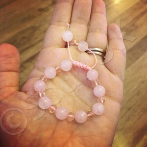 May include: A pink and clear crystal bracelet with a pink string closure. The bracelet is made with round beads and is shown on a hand.