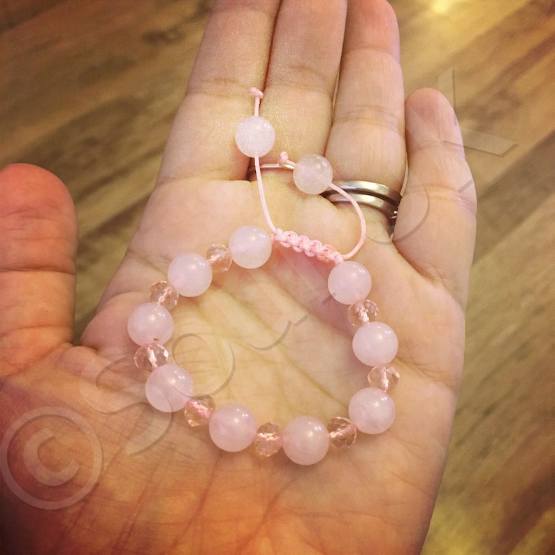 May include: A pink and clear crystal bracelet with a pink string closure. The bracelet is made with round beads and is shown on a hand.