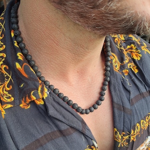 May include: A black lava rock beaded necklace worn by a person with a patterned shirt.