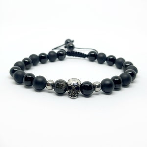 May include: Black onyx beaded bracelet with a silver skull charm. The bracelet has a black cord closure.