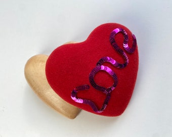 May include: A red felt heart with a pink sequin "LOVE" design on top of a wooden heart.