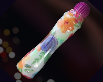 May include: A white marker with a purple cap and a floral design. The design features colorful flowers and leaves on a white background.