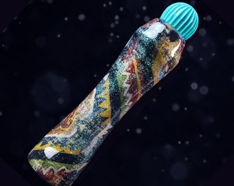 May include: A turquoise glitter marker with a colorful patterned design. The marker has a turquoise cap with a rounded top.
