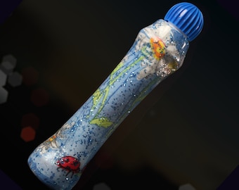 May include: A blue glitter marker with a white and green floral design and a ladybug. The marker has a blue cap with a white top.