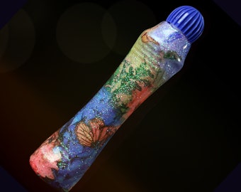 May include: A blue and purple glitter marker with a floral and butterfly design. The marker has a blue cap.