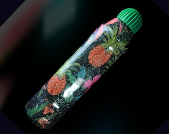 May include: A green and black glitter bottle with a pineapple and floral design. The bottle has a green plastic cap.