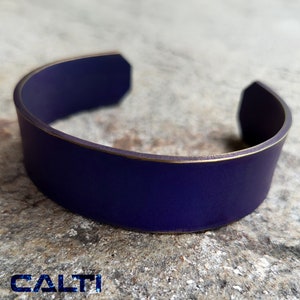 May include: A purple titanium bracelet with a gold edge. The bracelet is made by CALTI TITANIUM EDC.