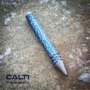 May include: A blue and silver pen with a textured, dotted pattern. The pen has a silver tip and a silver top. The text "CALTI TITANIUM EDC" is visible in the image.