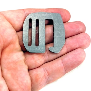 Puede incluir: Una hebilla de metal plateado con tres ranuras y un gancho. La hebilla está en una mano.