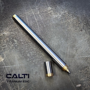 May include: A silver titanium pen with gold detailing and a separate cap. The pen rests on a textured grey surface. The text "CALTI TITANIUM EDC" is displayed in the bottom left corner.
