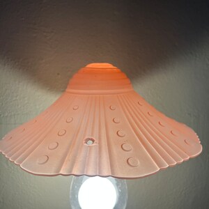 Peut inclure: Un abat-jour de lampe en verre rose avec un bord festonn&eacute; et une ampoule blanche. L'abat-jour est orn&eacute; d'un motif de petits cercles autour du bord.