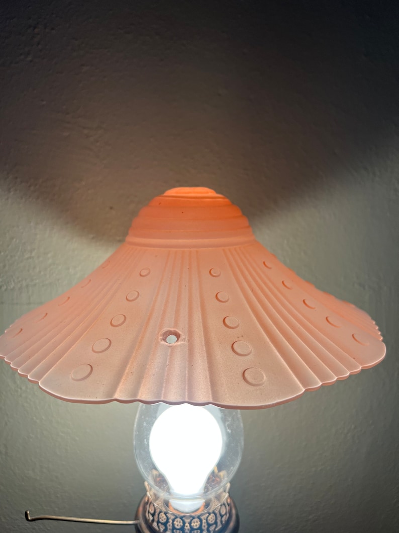 Peut inclure: Un abat-jour de lampe en verre rose avec un bord festonn&eacute; et une ampoule blanche. L'abat-jour est orn&eacute; d'un motif de petits cercles autour du bord.