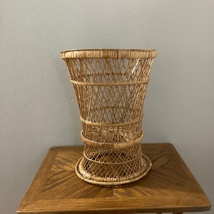 May include: A natural woven wicker basket with a wide, round opening and a tall, cylindrical shape. The basket is made of light brown wicker and has a natural, rustic look.