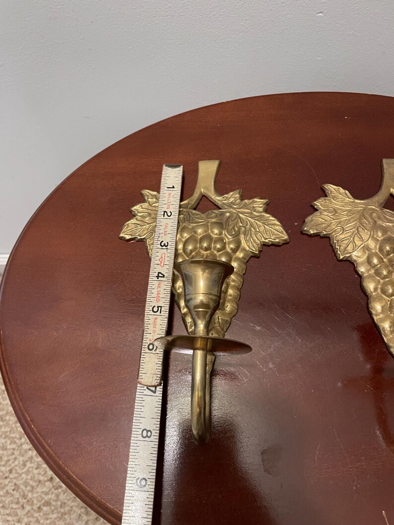 May include: A pair of gold-toned brass candle holders with a grapevine design. Each holder is approximately 6 inches tall.
