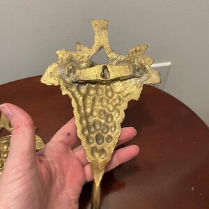 May include: A pair of gold-tone metal grapevine hooks. Each hook features a detailed grape cluster design.