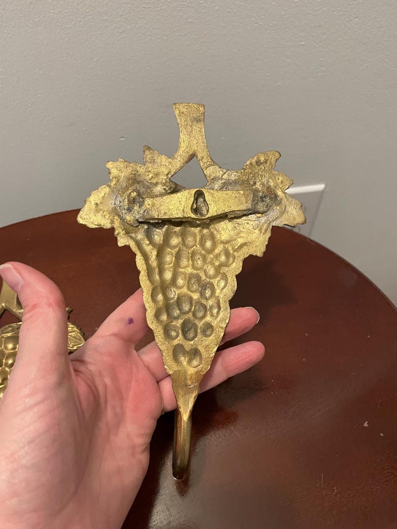 May include: A pair of gold-tone metal grapevine hooks. Each hook features a detailed grape cluster design.