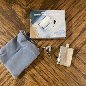 Puede incluir: Flacon de perfume plateado con embudo, en una bolsa de terciopelo gris, y una caja que dice "Silver Plated Perfume Flacon with Funnel".