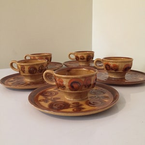 May include: Set of five brown and orange ceramic teacups and saucers with a swirling pattern.