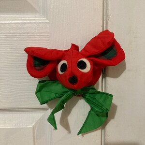 Może przedstawiać: Czerwona mysz z filcu z zielonymi kratkowanymi uszami i zieloną kokardką. Mysz jest ozdobą świąteczną.