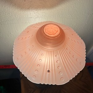 Peut inclure: Un abat-jour de lampe en verre rose avec un bord festonn&eacute; et un motif floral au centre. L'abat-jour a une surface textur&eacute;e avec de petits points.
