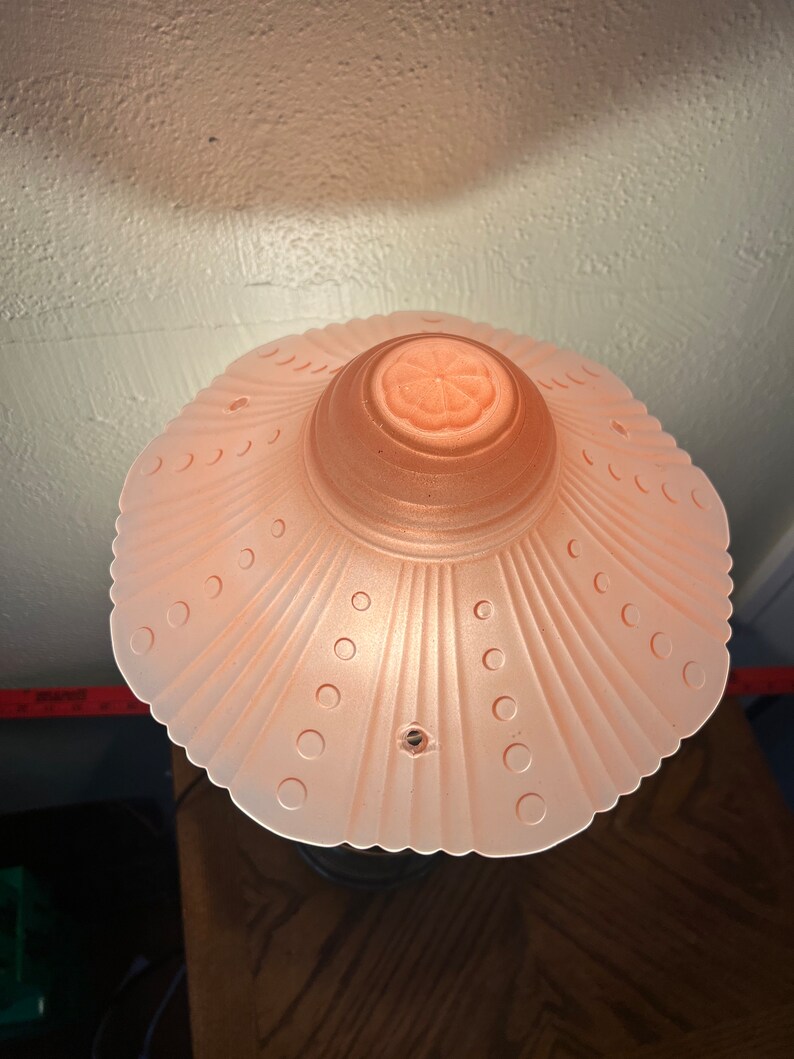 Peut inclure: Un abat-jour de lampe en verre rose avec un bord festonn&eacute; et un motif floral au centre. L'abat-jour a une surface textur&eacute;e avec de petits points.