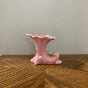 Może przedstawiać: Różowy ceramiczny wazon o unikalnym, stylizowanym wzorze. Wazon ma kształt trąbki z zakrzywioną podstawą.