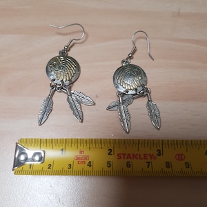 Può includere: Orecchini d'argento con un ciondolo a forma di copricapo nativo americano color oro e tre ciondoli a forma di piuma che pendono da ogni orecchino.