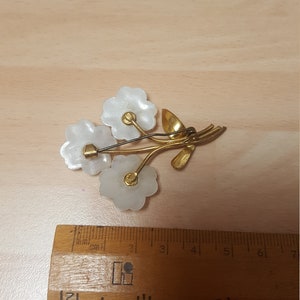 May include: A gold tone brooch with three white flower-shaped pieces and a gold stem with leaves.