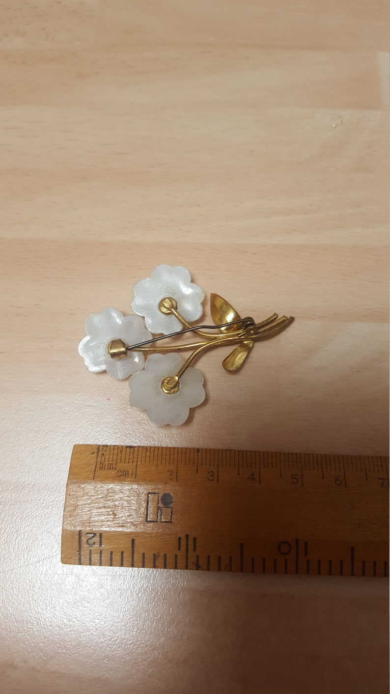 May include: A gold tone brooch with three white flower-shaped pieces and a gold stem with leaves.