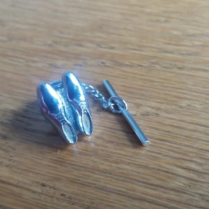 May include: Silver tie tack featuring a pair of shoes with a bar pin.