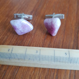 Puede incluir: Un par de gemelos con detalles de piedras rosas y blancas. Las piedras están engastadas en metal plateado.